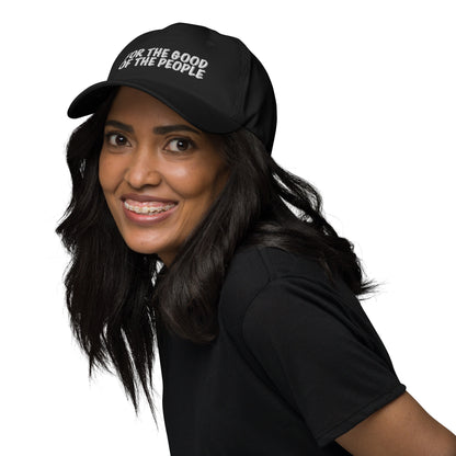 Girl wearing black shirt and black dad hat with for the good of the people embroidered in white on the front of hat.